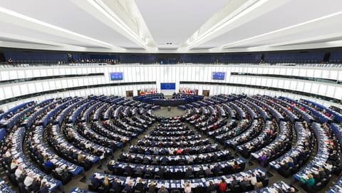 Vue plongeante sur l’hémicycle du Parlement européen à Strasbourg pendant une séance plénière, les députés installés en cercles concentriques autour d’une tribune surmontée du drapeau européen et des drapeaux des États membres.