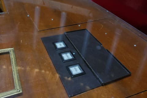 A voting console set into a mahogany desk in the French National Assembly chamber, its three buttons labeled "abst.", "contre" and "pour", in front of a red velvet bench.