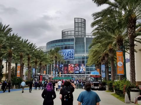 La façade vitrée de l’Anaheim Convention Center un jour de BlizzCon, le logo bleu du salon au-dessus des affiches de Warcraft, Diablo, Hearthstone et Overwatch, des palmiers de chaque côté et des visiteurs en tee-shirt noir qui remontent l’allée.